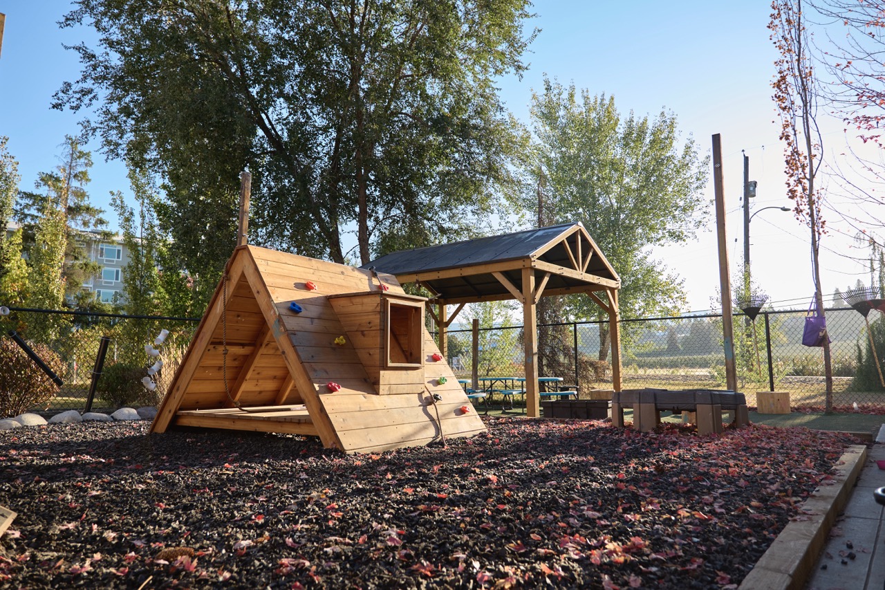 A Bella Vita outdoor play yard with wooden climbing structures and trees
